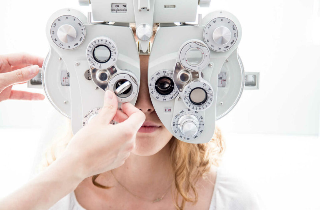 A young woman patient looking through a phoropter while hands are seen adjusting the lenses.