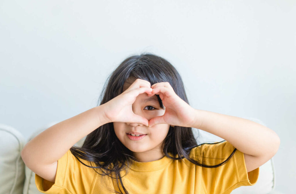 A young girl using her hands to make a heart around her eye, showing the importance of eye health in young kids