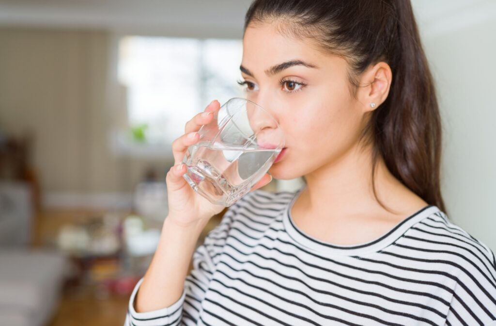 A young woman in a striped shirt drinking a glass of water.