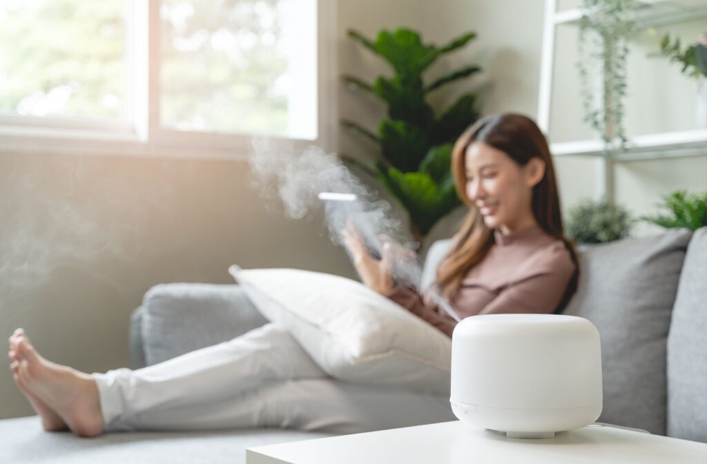A woman sits at home on the couch working on her tablet with a humidifier next to her to keep moisture in the air.