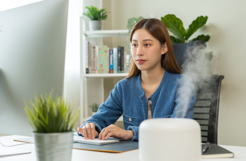 A young woman working in her office with a humidifier on her desk to help bring moisture into the air to relieve her dry eyes.