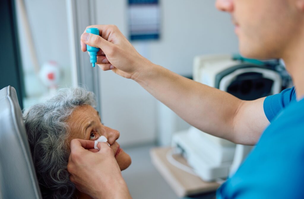 An optometrist administers dilating eye drops to their mature patient during their dilation exam.