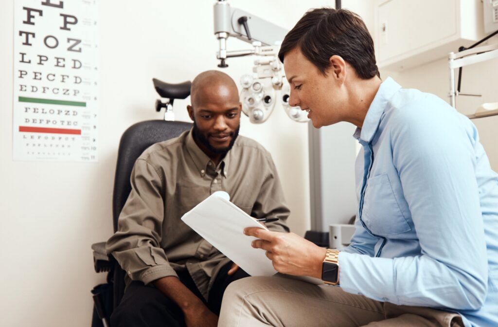 An optometrist holding a clipboard, writing a prescription and explaining the results after an eye exam.