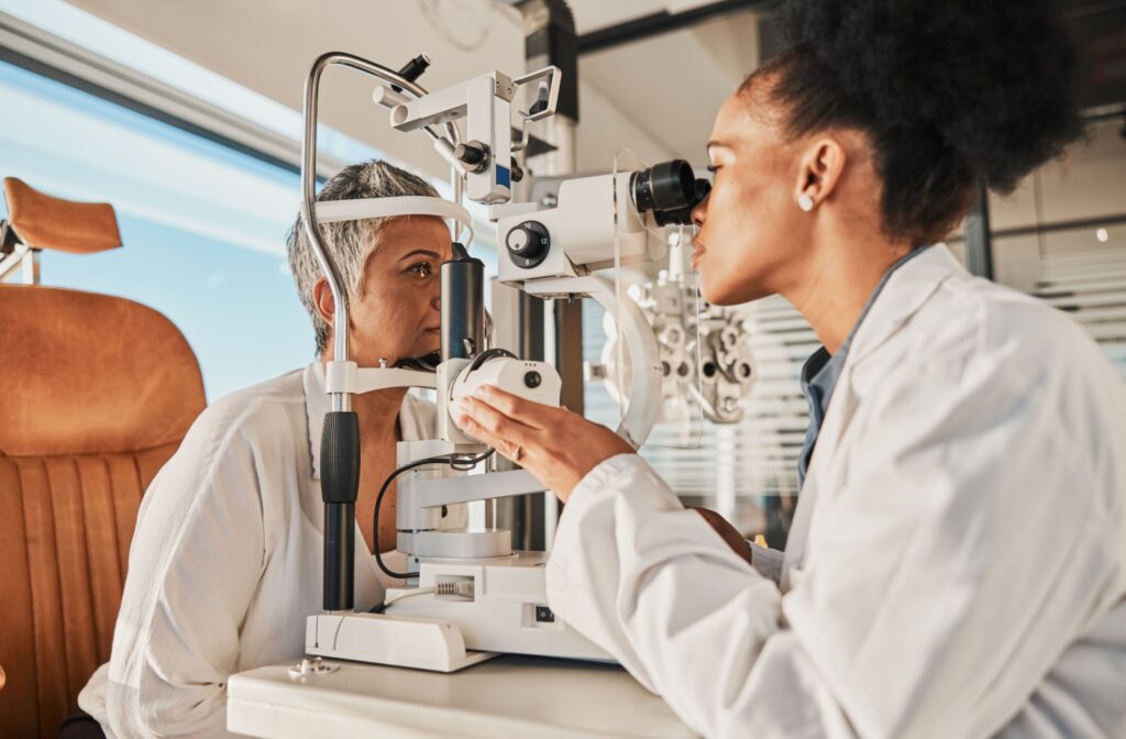 An older adult smiling during an eye exam while an optometrist checks their eyes with a slit lamp.