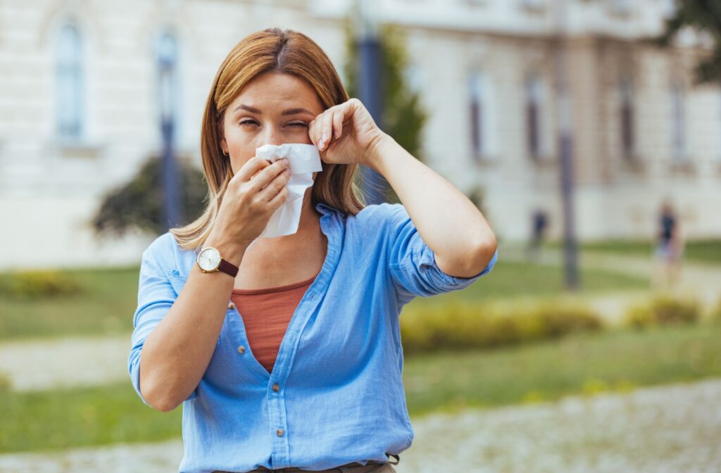 A person with pollen allergies rubs the corner of their dry eyes while they blow their nose.