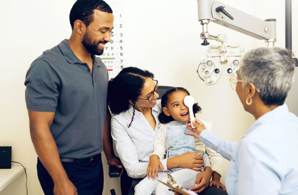 A child smiles at an eye doctor while sitting in her moms lap at the optometrists office.