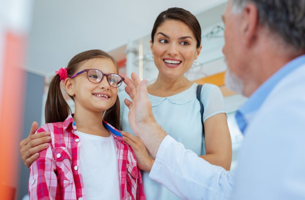 A mom and her daughter talking with an eye doctor who is adjusting the daughters glasses.