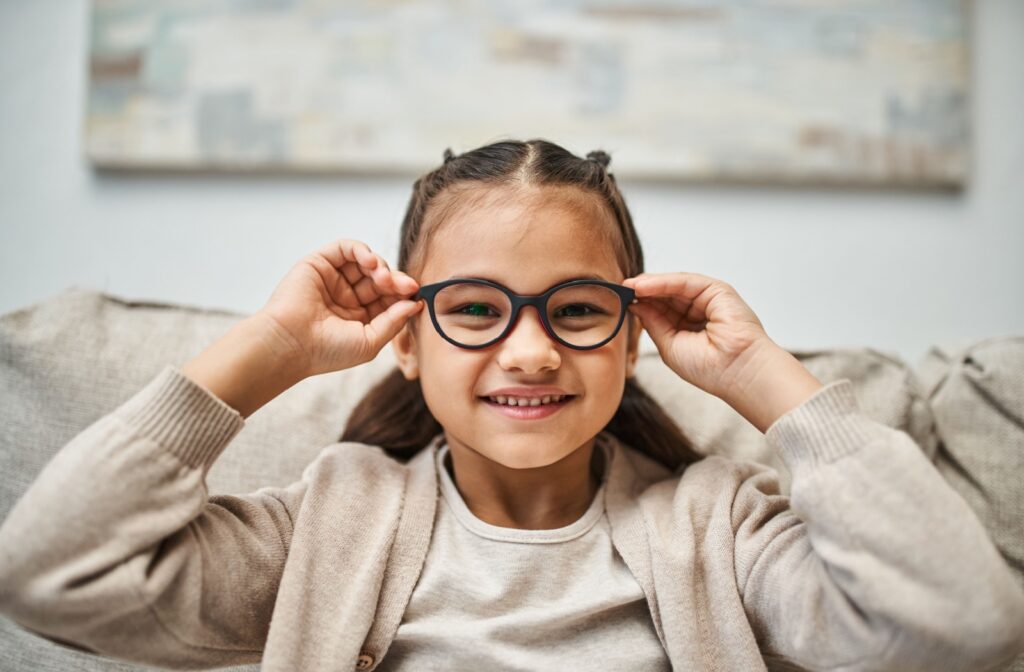 A young child smiles as they put a pair of glasses on for their myopia
